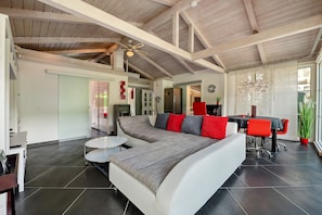 A modern living room with a sectional sofa, a dining table, and a ceiling fan.