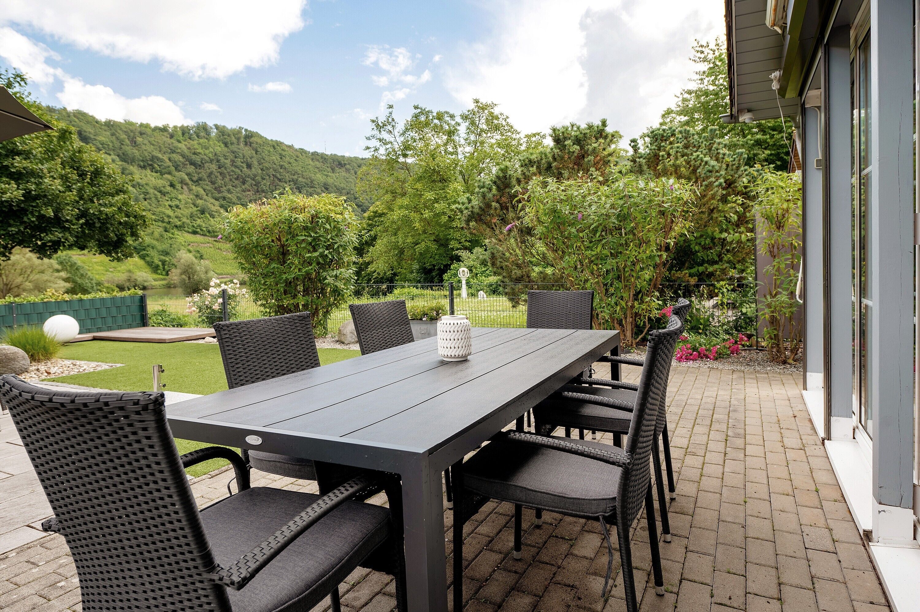 Un patio con tavolo e sedie, un vaso bianco e vista su un paesaggio verde.