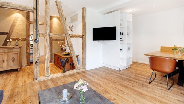 A modern living room with a wooden ladder, a flat-screen TV, white cabinets, and a dining area. - Ferienwohnung Mühlengrund, 92 qm, 3 Schlafzimmer, max. 6 Personen (Kirchhundem)