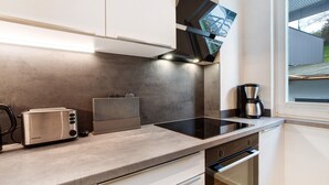 A modern kitchen with a built-in oven, a coffee maker, and a view of the outside through a window. - Ferienwohnung Mühlengrund, 92 qm, 3 Schlafzimmer, max. 6 Personen (Kirchhundem)