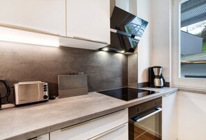 A modern kitchen with a built-in oven, a coffee maker, and a view of the outside through a window. - Ferienwohnung Mühlengrund, 92 qm, 3 Schlafzimmer, max. 6 Personen (Kirchhundem)