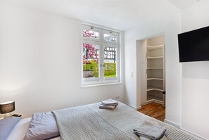 Ein Schlafzimmer mit Bett, Fenster mit Blick auf Grünflächen, Nachttisch mit Lampe und Kleiderschrank.