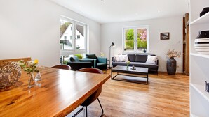 A modern living room with a wooden dining table, a sofa, and a coffee table. - Ferienwohnung Mühlengrund, 92 qm, 3 Schlafzimmer, max. 6 Personen (Kirchhundem)