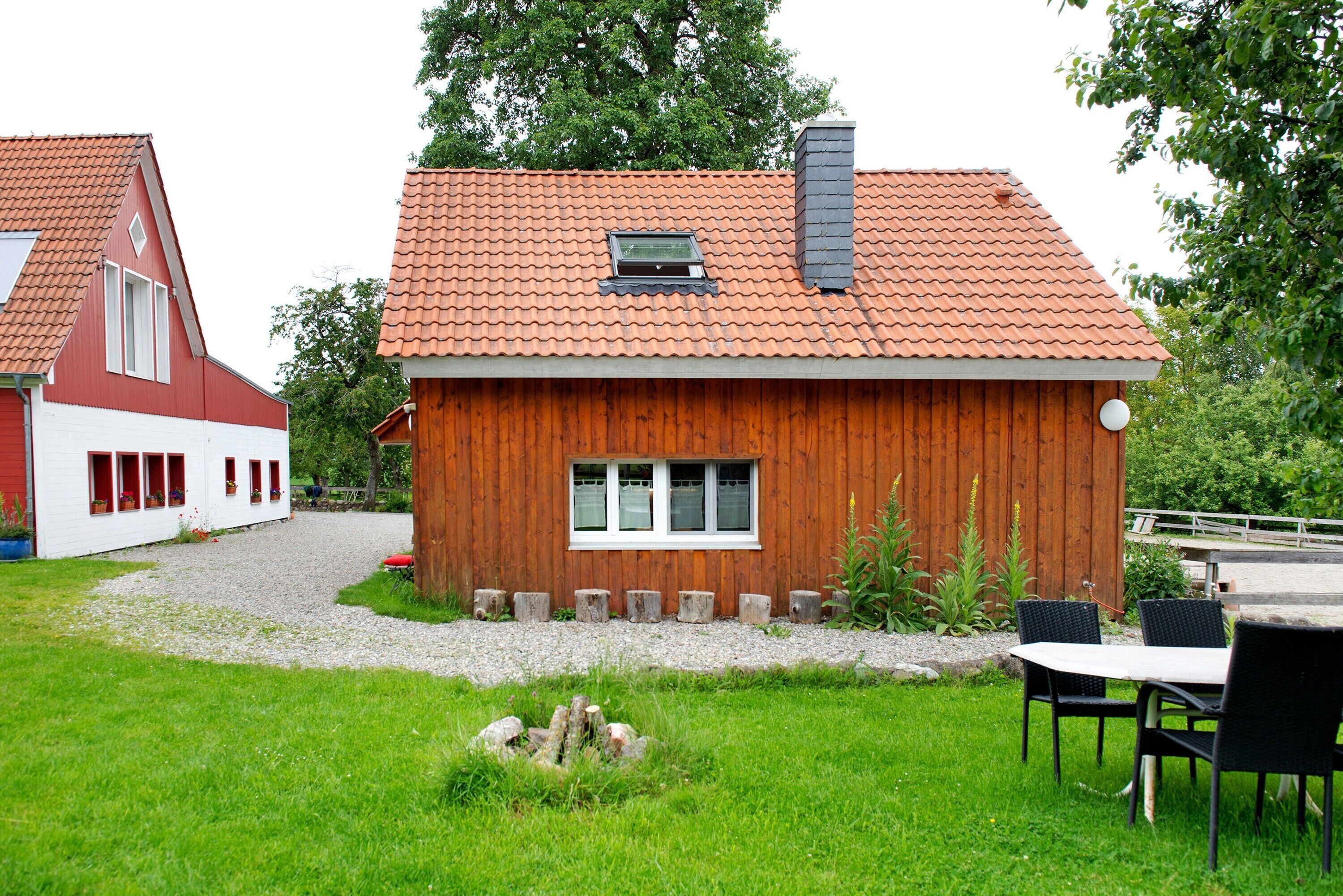 A wooden house with a tiled roof, a window, and a gravel driveway.