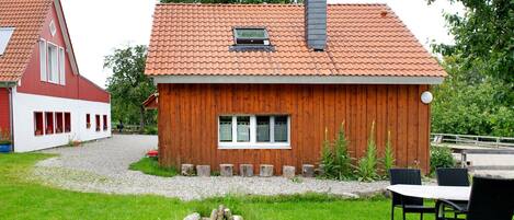 A wooden house with a tiled roof, a window, and a gravel driveway.