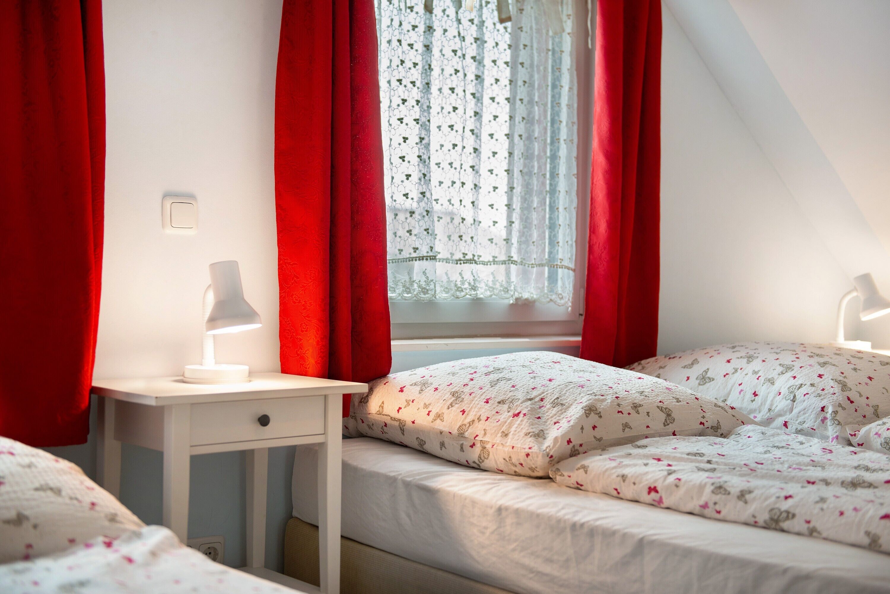 Une chambre à coucher avec un lit, une table de chevet avec une lampe et une fenêtre avec des rideaux.