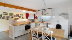Une cuisine avec des meubles blancs, un plan de travail en bois, une table à manger avec des chaises et un four blanc.