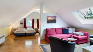 Une pièce avec un plafond en pente, un canapé rose, un lit avec deux oreillers, une petite table avec un vase et un tableau au mur.