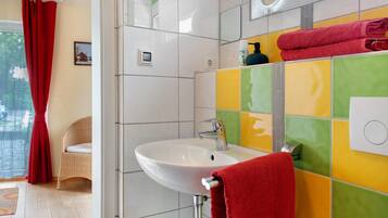 A bathroom with a white sink, colorful tiles, a red towel, and a wicker chair.