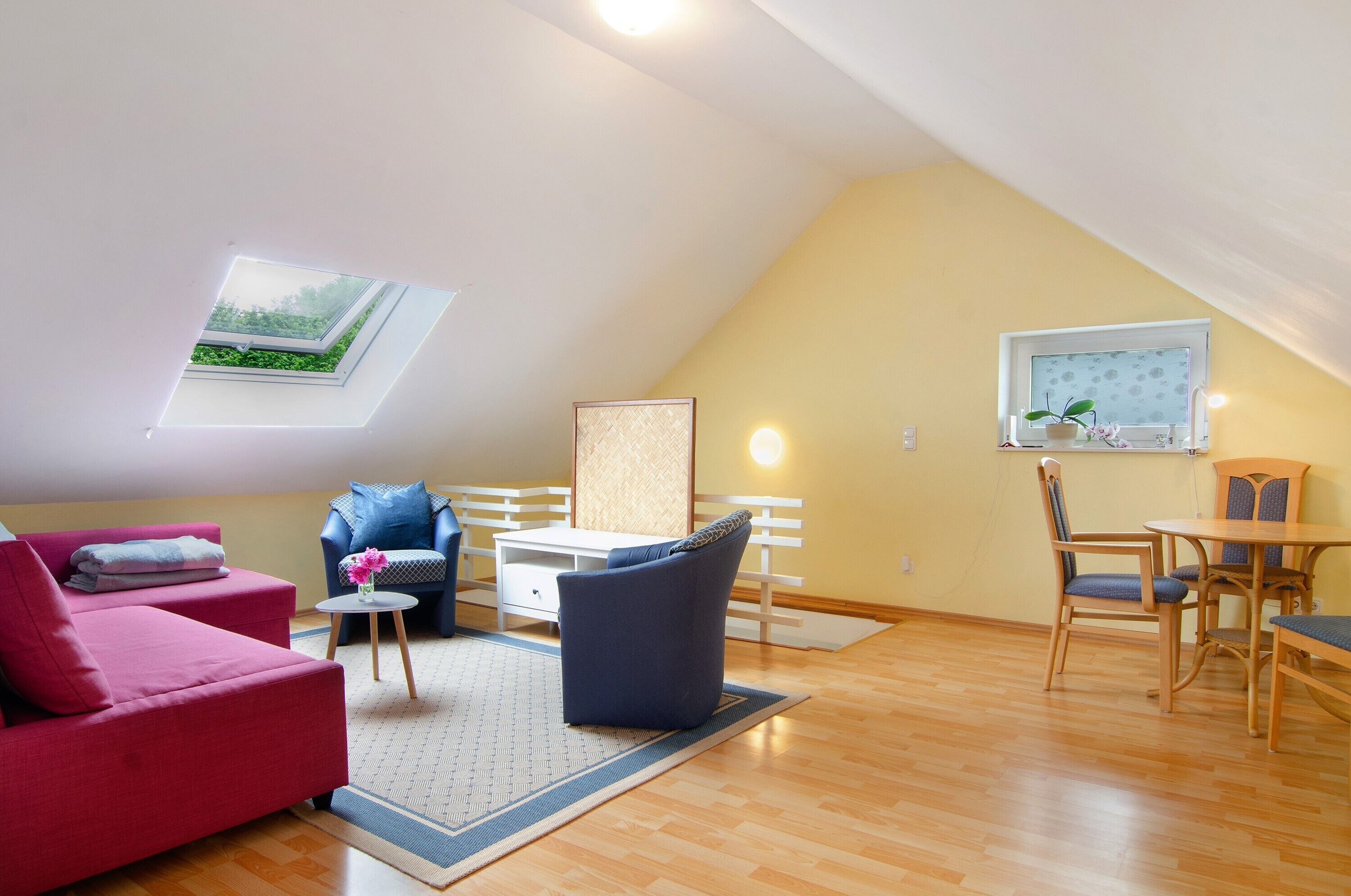 Ein gemütliches Loft mit Dachfenster, einem Essbereich und einem Wohnraum mit Sofa und Sesseln.