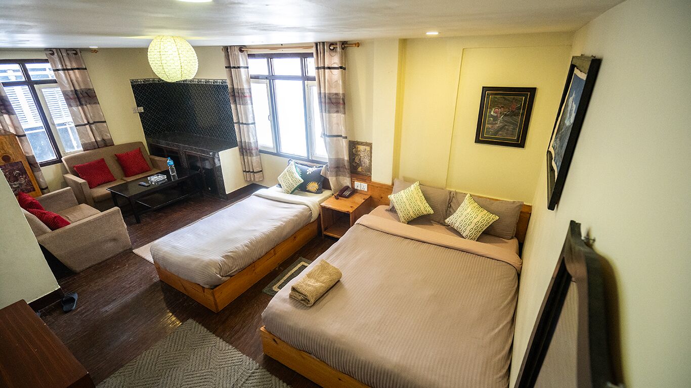 A hotel room with two single beds, a sofa, a small table, a fireplace, and a window with curtains.