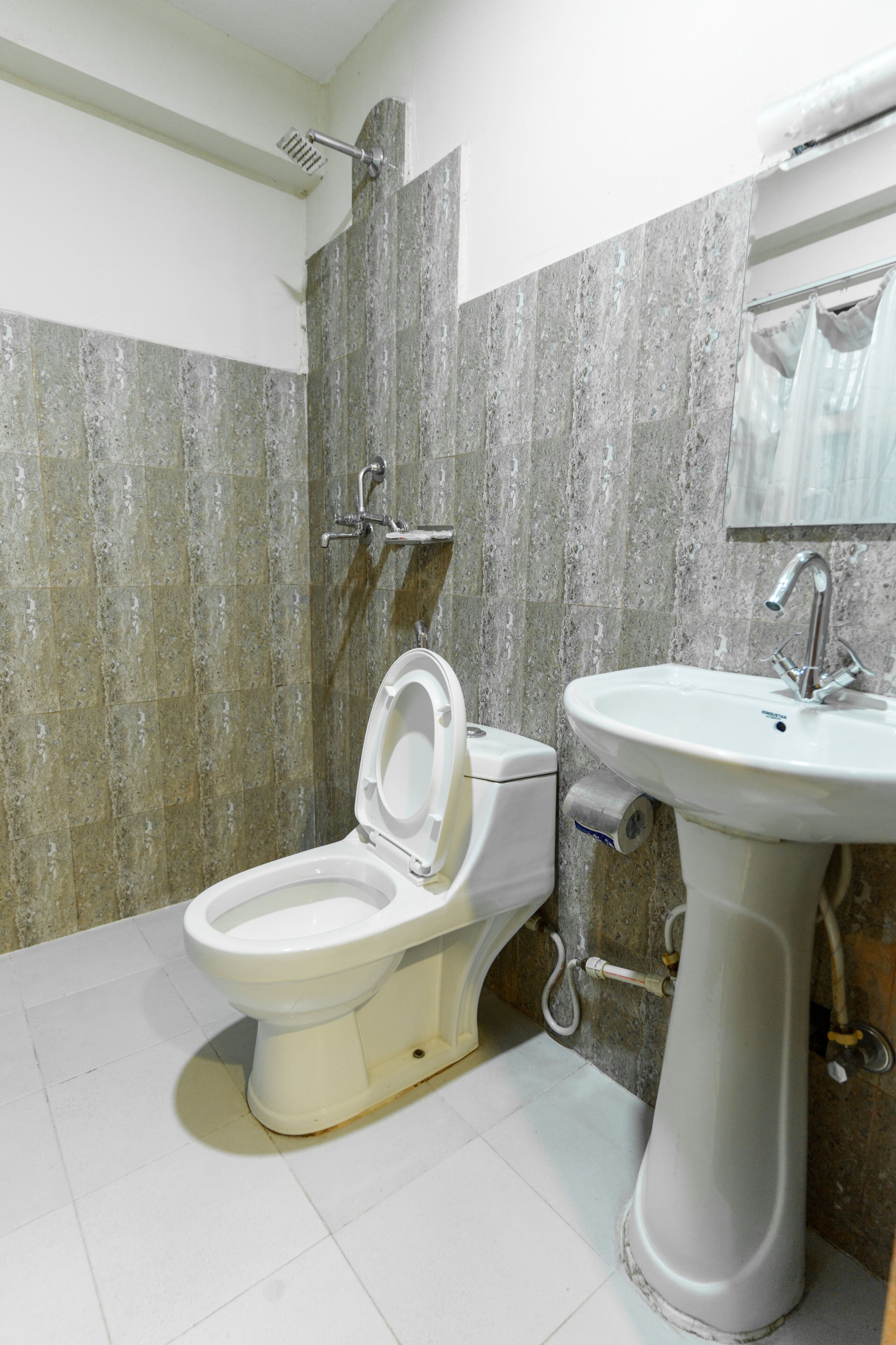A bathroom with a toilet and sink, both in white, against a backdrop of grey stone tiles.