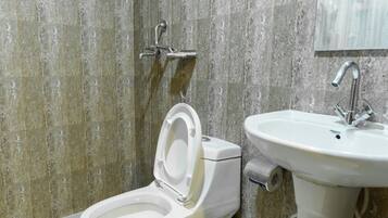 A bathroom with a toilet and sink, both in white, against a backdrop of grey stone tiles.