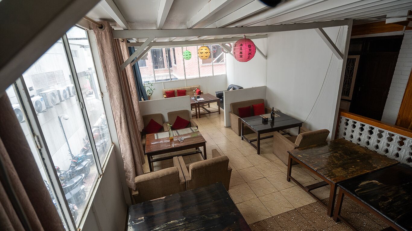 Un espace repas avec des tables et des chaises, un canapé et une vue sur la rue grâce à de grandes fenêtres.
