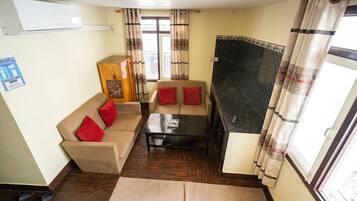 Un espacio habitable compacto con sofá, mesa de centro y un mueble bajo. Se ve una ventana con cortinas, y una pared de azulejos negros.