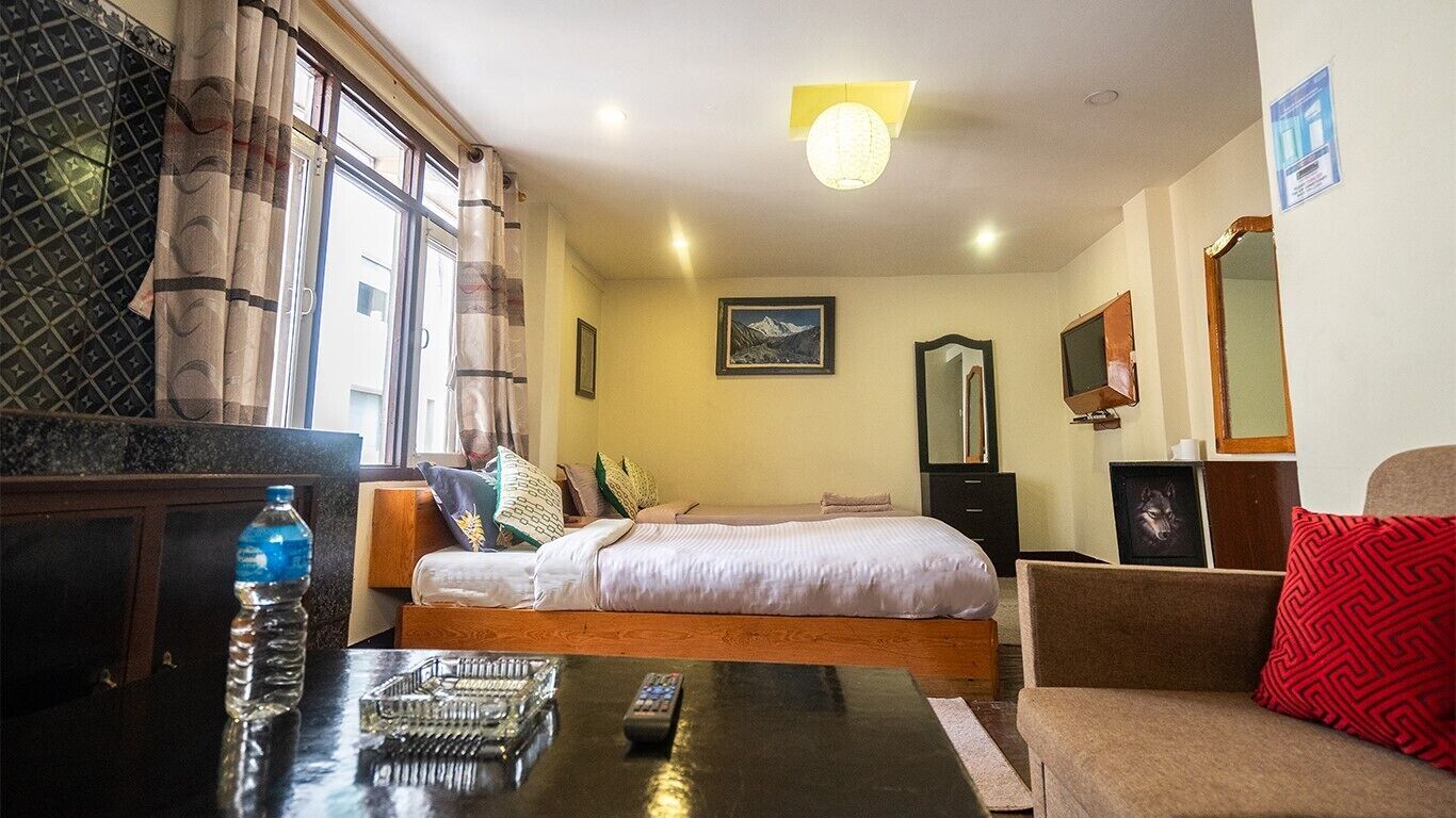 A hotel room with a bed, a sofa, a table with a remote control, a water bottle, and a mirror.