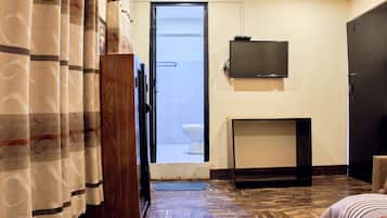 Une chambre d’hôtel avec une armoire en bois, un téléviseur fixé au mur, une petite table et une porte donnant sur une salle de bain.