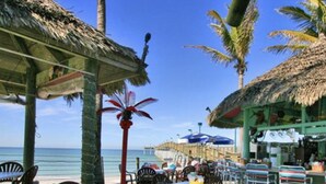 Un restaurant situé en bord de mer, avec une terrasse, des palmiers et une vue sur l’océan.