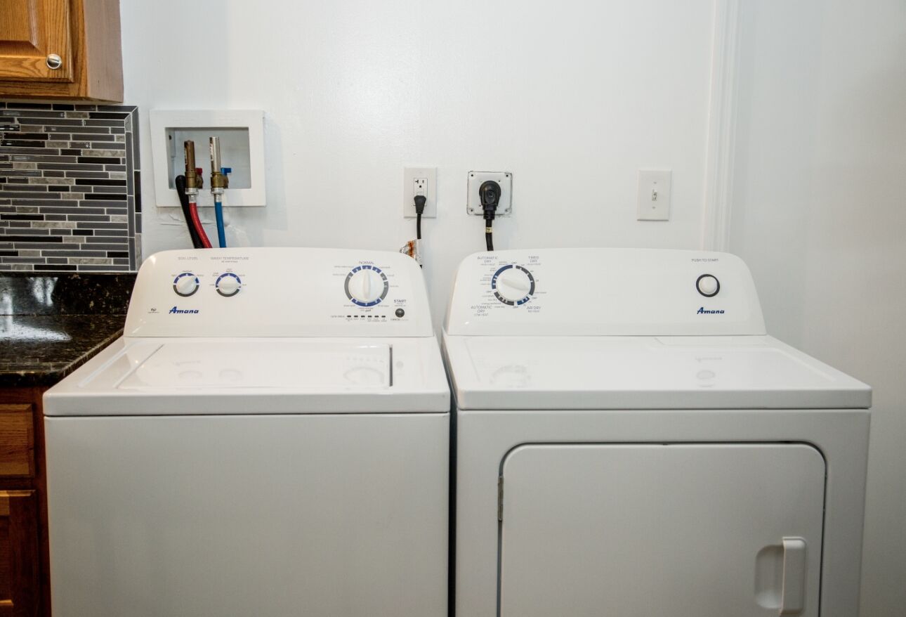Two white front-loading Amana washing machines side by side with control panels, connected to a power outlet.