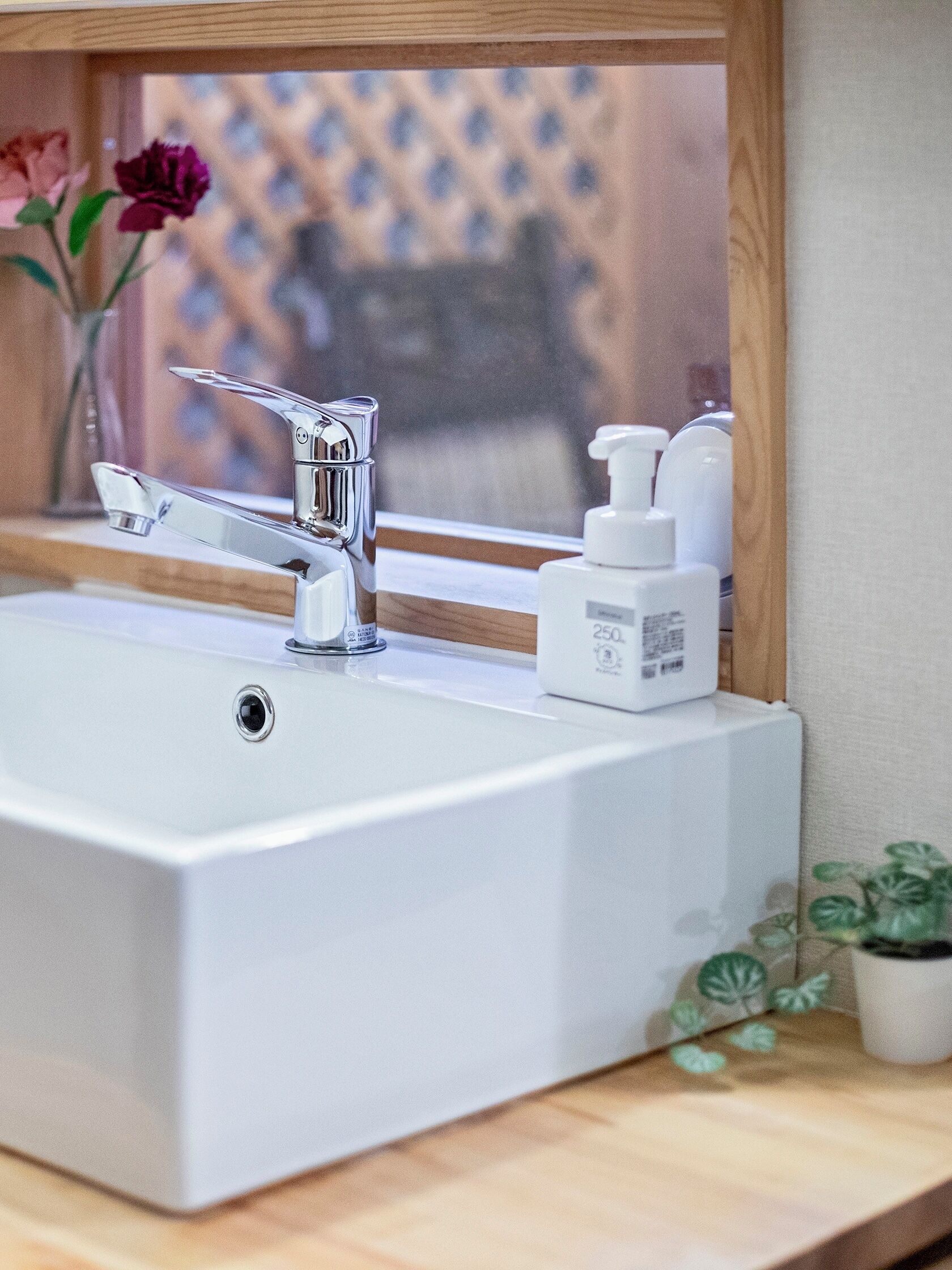 A bathroom sink with a chrome faucet, a mirror above it, and a window with a view of a fence and flowers outside.
