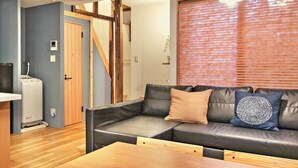 Una sala de estar moderna con un sofá, una mesa de madera y un amplio ventanal con persianas.