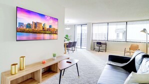 A modern living room with a cityscape painting, a sofa, a coffee table, and a dining area with chairs and a table.