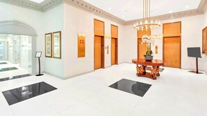 A spacious lobby with a central round table, a chandelier, and a reception desk.