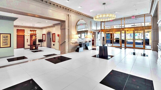 A spacious lobby with a high ceiling, a grand chandelier, and a large mirror reflecting the interior.
