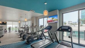 A modern gym with treadmills, elliptical machines, and weight stations. Large windows offer views of the city. - Unwind in Your Amazing City View Apartment (Miami)