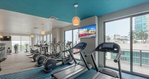 A modern gym with treadmills, elliptical machines, and weight stations. Large windows offer views of the city. - Unwind in Your Amazing City View Apartment (Miami)