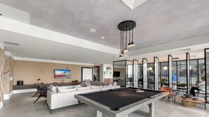 Una sala de estar moderna con mesa de billar, zona de estar y ventanas amplias.
