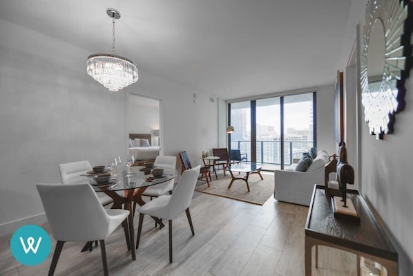 Un salon moderne avec un coin repas, de grandes fenêtres et un lustre.