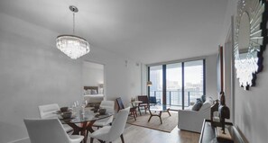 A modern living room with a dining area, large windows, and a chandelier. - Unwind in Your Amazing City View Apartment (Miami)
