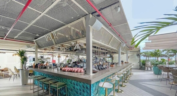 A modern bar area with a bar counter, multiple stools, and a ceiling with a grid pattern. - Unwind in Your Amazing City View Apartment (Miami)
