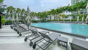 A swimming pool area with lounge chairs and umbrellas, surrounded by palm trees and a modern building. - Unwind in Your Amazing City View Apartment (Miami)