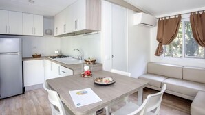 Una cocina moderna con armarios blancos, estufa integrada y un comedor con mesa de madera y sillas blancas.