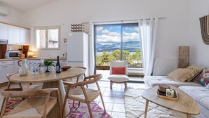 Eine moderne Küche mit weißen Schränken, einer Mikrowelle und einem Kühlschrank. Es gibt eine Essecke mit einem Holztisch und Stühlen sowie einen Blick auf Berge durch große Fenster.