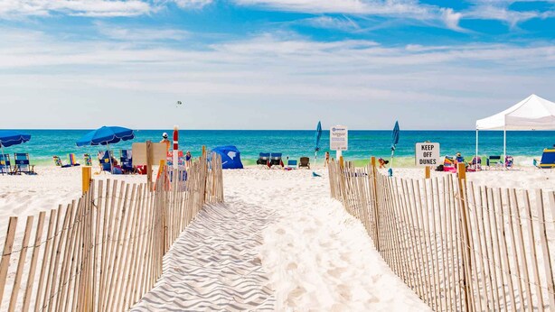 Ein Strand mit einer Holzlattenveranda, die zum Wasser führt, Strandkörbe, Sonnenschirme und einem Zelt.