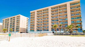 Ein Hotel direkt am Strand mit mehreren Etagen, Balkonen und Palmen.