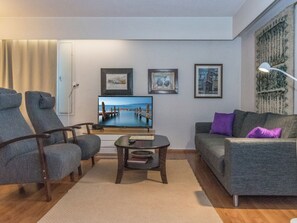 A living room with a television, two armchairs, a sofa, a coffee table, and a rug.