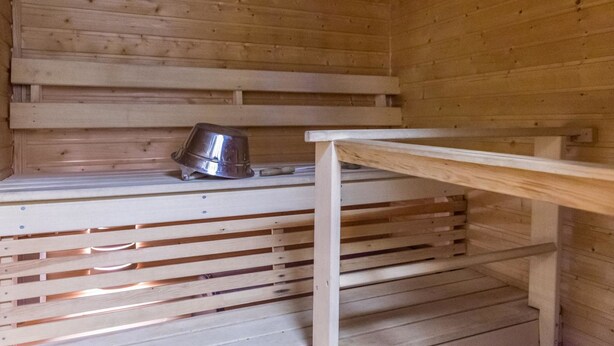 A wooden sauna room with a bench and a metal container. - Saariseläntie 8 b 7 by Interhome (Inari)