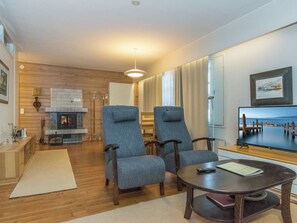 A living room with two blue armchairs, a wooden coffee table, a fireplace, and a television displaying a cityscape. - Saariseläntie 8 b 7 by Interhome (Inari)