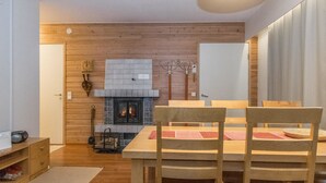 A cozy room with a fireplace, wooden walls, a dining table with chairs, and a ceiling light. - Saariseläntie 8 b 7 by Interhome (Inari)