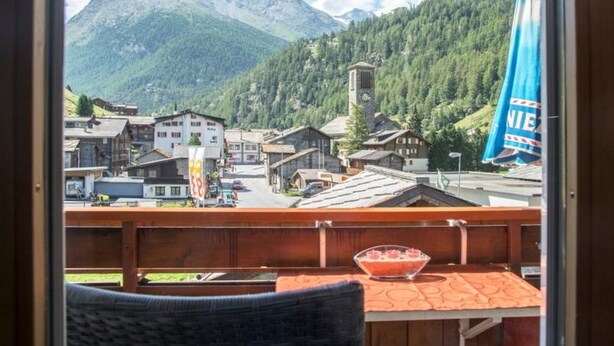 A balcony with a wooden railing, a table with a glass bowl, and a mountain view. - Wiedersehen by Interhome (Saas-Grund)