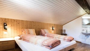 A bedroom with a wooden ceiling, a bed with patterned bedding, a nightstand, and a bathroom with a sink and mirror. - Wiedersehen by Interhome (Saas-Grund)