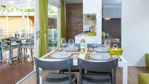 A modern dining area with a table set for four, a kitchen area with a stove and sink, and a view of the outdoors through large windows. - Fashion by Interhome (Castiglione della Pescaia)