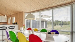 Zona de menjador moderna amb taula blanca, cadires de colors i una finestra gran amb persianes.