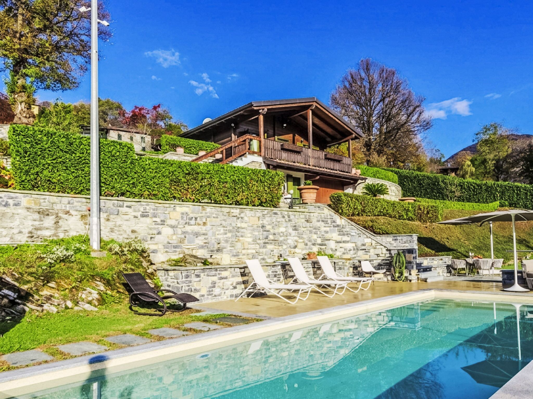 Ein Poolbereich mit Liegestühlen, einer Steinmauer und einem Gebäude mit Balkon.