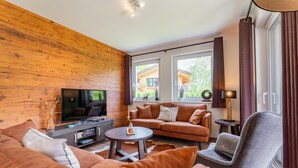 A modern living room with a wooden wall, a sofa set, a TV, a coffee table, and a chair.