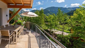 A balcony with a wooden ceiling, outdoor furniture, and a view of a mountainous landscape.